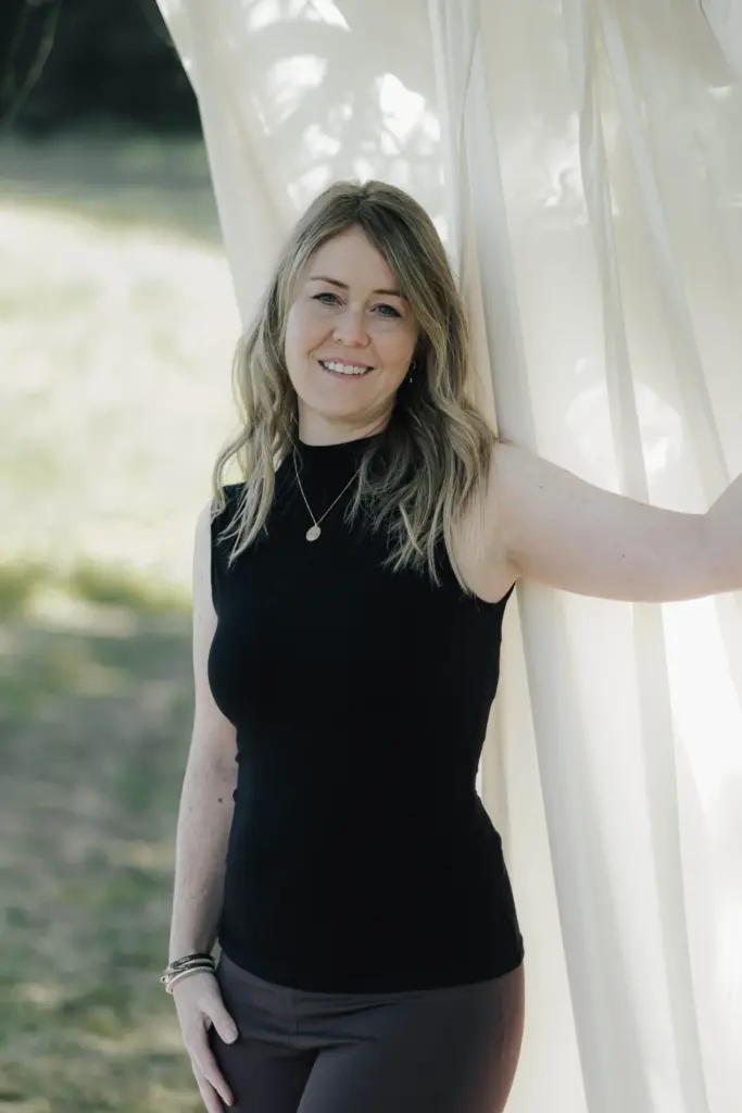 Nadine Bauer von Mamalove & Nature steht vor einem weißen Vorhang und blickt in die Kamera. Nadine bietet mit Mamalove and nature Kurse in der Schwangerschaft und für die Rückbildung an.