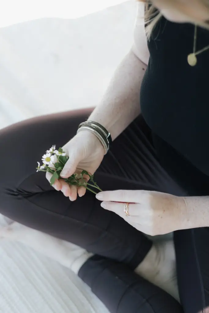 Nadine Bauer von Mamalove and Nature ist schwarz angezogen, sitzt im Schneidersitz und hält eine Blume in der Hand. Nadine bietet Coachings und Kurse zu den Themen Schwangerschaft und Rückbildung an.