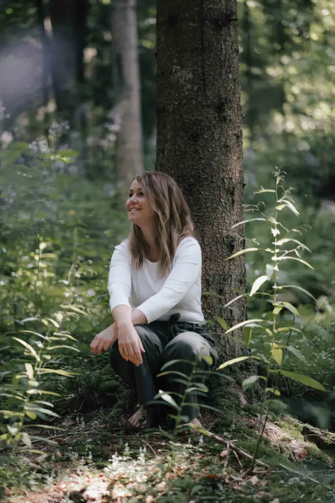 Nadine Bauer, Inhaberin von Mamalove and Nature, sitzt im Wald an einem Baum angelehnt.